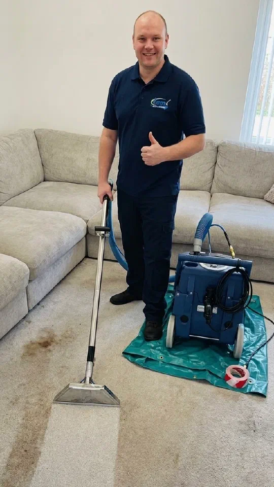Mark standing beside his carpet cleaning machine, thumbs up, with a stripe of cleaned carpet in front of him next to the dirty carpet still to be done.