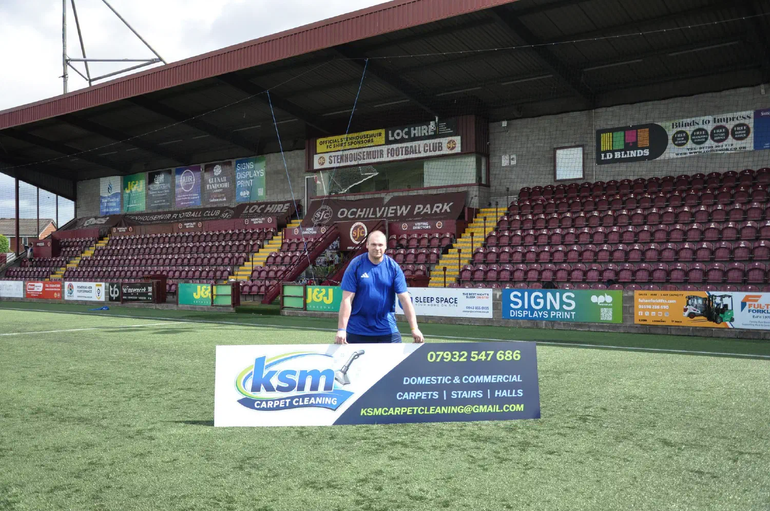 Mark holding his KSM Carpet Cleaning advertising board on the pitch at Ochilview Park.