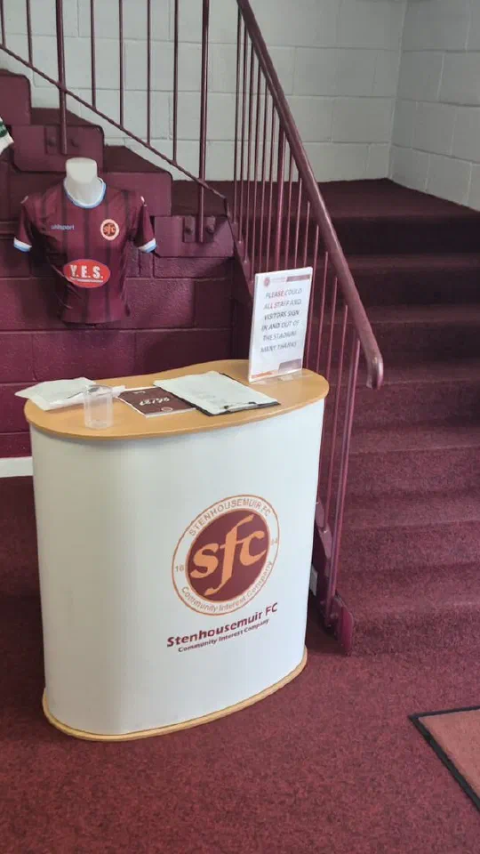 The reception at Ochilview Park, with the Stenhousemuir FC desk and the club crest on the floor mat.